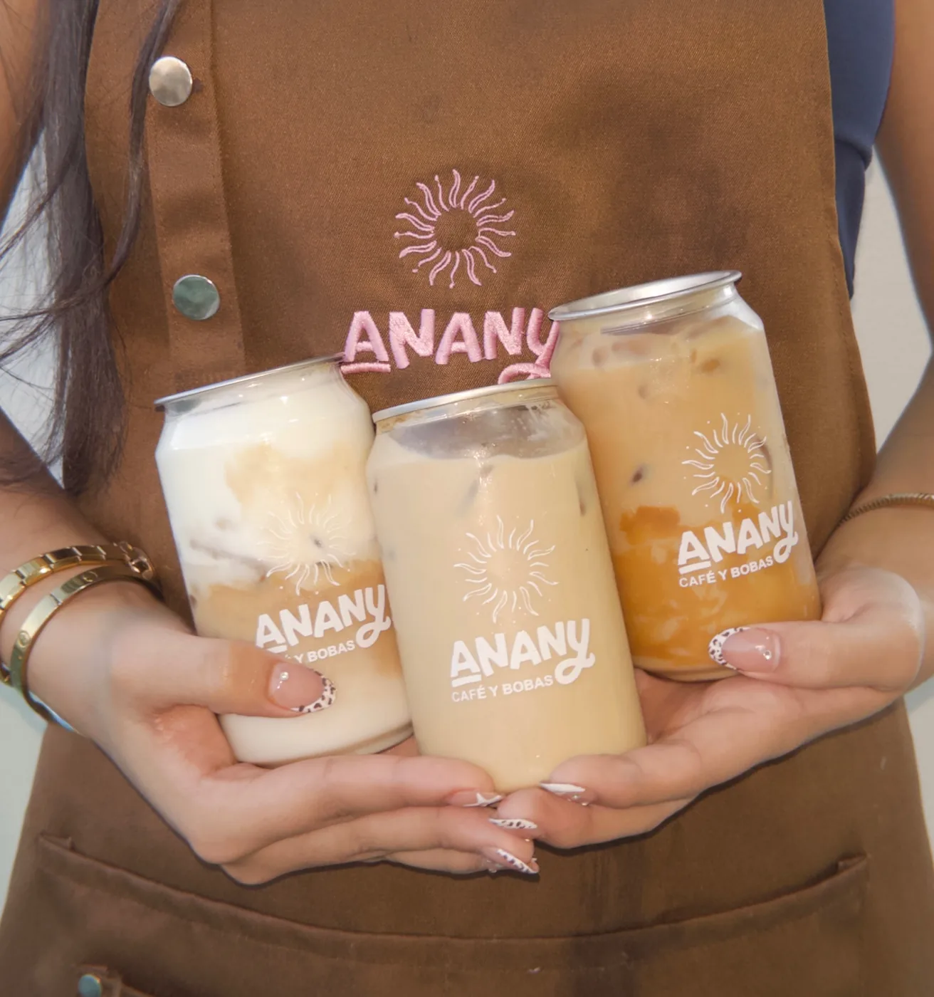 Tres latitas de Anany en sus tres tamaños, sostenidas frente al mandil de la casa